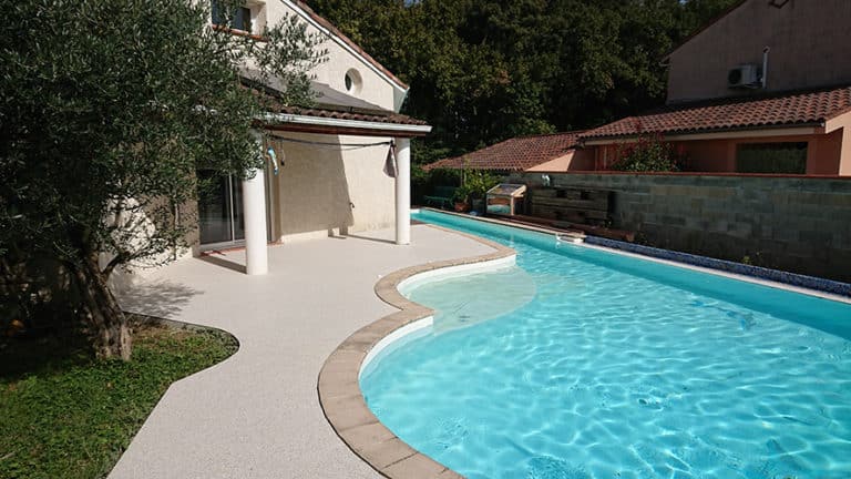Réalisation à Toulouse d'une terrasse en résine moquette de pierre au bord d'une belle piscine.